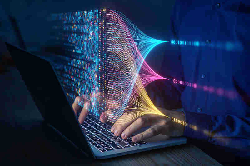 Technician typing on a laptop above which float blue, magenta and yellow lines that intersect to generate a data visualization